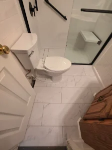 Tub-to-shower bathroom remodel in Chesapeake Beach MD with white shower walls, black fixtures, glass enclosure, and fold-down seat